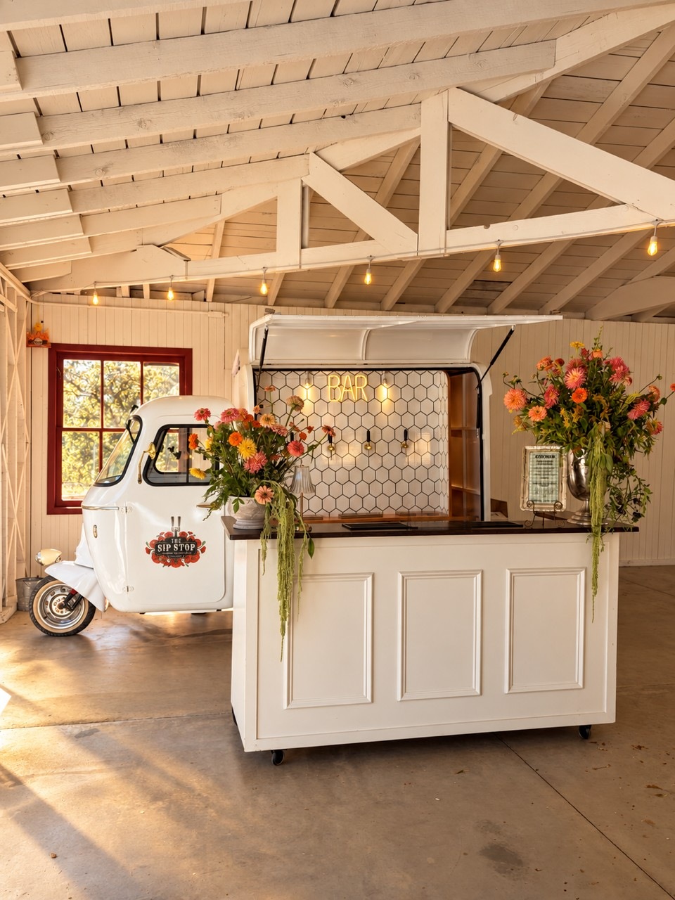 White Piaggio and portable bar with flowers inside a white-beamed venue